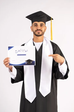 Pointing the index finger at the certificate, achieving the dream of success, a university occasion and celebration, celebrating the completion of university studies, the concept of diligence and excellence, a portrait of a smiling young Arab Gulf Emirati graduate wearing a graduation gown looking at the camera with an expression of happiness, white background