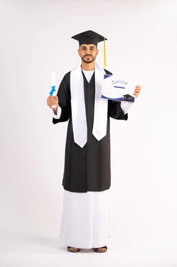 تعابير السعادة والسرور، مناسبة واحتفال جامعي، الاحتفال بإنهاء الدراسة الجامعية، مفهوم الاجتهاد والتفوق، بورتريه لشاب خريج عربي خليجي اماراتي مبتسم يرتدي عباءة التخرج يمسك بيده الشهادة، الوصول لحلم النجاح، الجسم بالطول الكامل، خلفية بيضاء