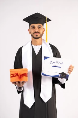 الحصول على الشهادة بتعابير الفرح، الشعور بالفخر والثقة بالنفس، الاحتفال بالنجاح وانهاء الدراسة الجامعية، مفهوم التفوق والاجتهاد، بورتريه لشاب خريج عربي خليجي اماراتي يرتدي قبعة وثوب التخرج يمسك بيده هدية بايماءات السعادة،، خلفية بيضاء