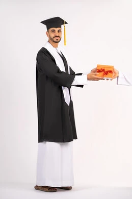 تقديم الهدايا بتعابير الفرح، الشعور بالفخر والثقة بالنفس، الاحتفال بالنجاح وانهاء الدراسة الجامعية، مفهوم التفوق والاجتهاد، بورتريه لشاب خريج عربي خليجي اماراتي يرتدي قبعة وثوب التخرج يقوم بأخذ الهدية بايماءات السعادة، الجسم بالطول الكامل، خلفية بيضاء