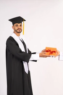 Giving gifts with expressions of joy, feeling proud and confident, celebrating success and finishing university studies, the concept of excellence and diligence, portrait of a young Arab Gulf Emirati graduate wearing a graduation cap and gown taking the gift with gestures of happiness, white background