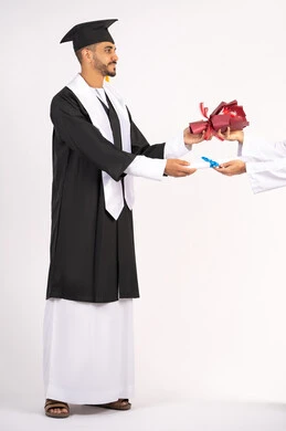 الشعور بالفخر والثقة بالنفس، استلام الشهادة بتعابير الفروح والسرور، الاحتفال بالنجاح وانهاء الدراسة الجامعية، مفهوم التفوق والاجتهاد، بورتريه لخريج عربي خليجي اماراتي يرتدي قبعة وثوب التخرج يقوم بأخذ باقة الورد بايماءات السعادة، الجسم بالطول الكامل، خلفية بيضاء