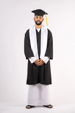 الاجتهاد والجد والنجاح، التقاط صور شخصية بثياب التخرج، الاحتفال بإنهاء المرحلة الجامعية، بورتريه لشاب خريج عربي خليجي اماراتي مبتسم يرتدي القبعة وعباءة التخرج يقف بأستقامة ينظر الى الكاميرا بتعابير الثقة بالنفس والسرور والسعادة، الجسم بالطول الكامل، خلفية بيضاء