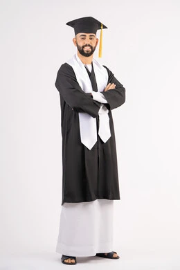 التقاط صور شخصية بثياب التخرج، الاحتفال بإنهاء المرحلة الجامعية، بورتريه لشاب خريج عربي خليجي اماراتي مبتسم يرتدي القبعة وعباءة التخرج يقف بأيدي متقاطعة ينظر الى الكاميرا بتعابير الثقة بالنفس، مفهوم التفوق والنجاح والاجتهاد، الجسم بالطول الكامل، خلفية بيضاء