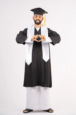 التعبير عن الحب والفرح، تشكيل اليدين على شكل قلب، التقاط صور شخصية بثياب التخرج، الاحتفال بإنهاء المرحلة الجامعية بنجاح وتفوق، بورتريه لشاب خريج عربي خليجي اماراتي مبتسم يرتدي القبعة وعباءة التخرج ينظر الى الكاميرا بتعابير السرور، الجسم بالطول الكامل، خلفية بيضاء