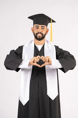تشكيل اليدين على شكل قلب، التعبير عن الحب والفرح، التقاط صور شخصية بثياب التخرج، الاحتفال بإنهاء المرحلة الجامعية بنجاح وتفوق، بورتريه لشاب خريج عربي خليجي اماراتي مبتسم يرتدي القبعة وعباءة التخرج ينظر الى الكاميرا بتعابير السرور، خلفية بيضاء