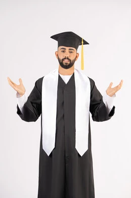 مفهوم التفوق والنجاح، التقاط صور شخصية بثياب التخرج، الاحتفال بإنهاء المرحلة الجامعية، بورتريه لشاب خريج عربي خليجي اماراتي مبتسم يرتدي القبعة وعباءة التخرج يرفع يديه لاعلى ينظر الى الكاميرا بتعابير السرور، خلفية بيضاء