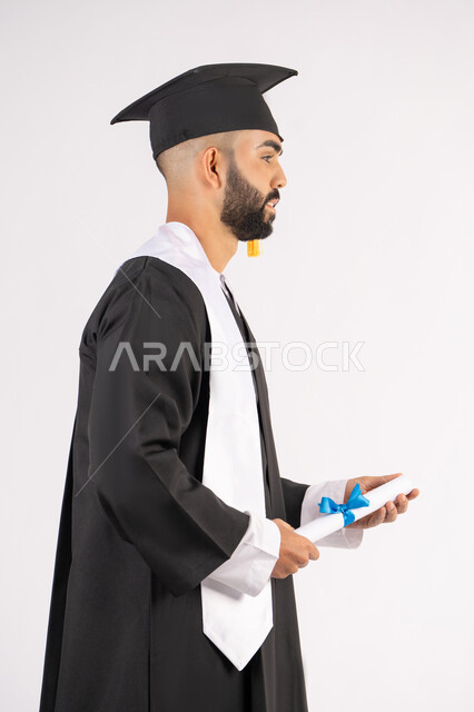 Feeling proud and confident, celebrating success and completing university studies, the concept of excellence and diligence, a portrait of an Arab Gulf Emirati graduate wearing a graduation cap and gown, standing straight with happy gestures, holding a certificate with expressions of joy and happiness, white background