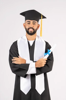 التقاط صور شخصية بثياب التخرج، الاحتفال بإنهاء المرحلة الجامعية، بورتريه لشاب خريج عربي خليجي اماراتي مبتسم يرتدي القبعة وعباءة التخرج يقف بأيدي متقاطعة ينظر الى الكاميرا بتعابير الثقة بالنفس، مفهوم التفوق والنجاح والاجتهاد، خلفية بيضاء
