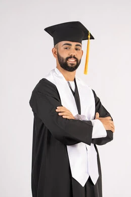 التقاط صور شخصية بثياب التخرج، الاحتفال بإنهاء المرحلة الجامعية، بورتريه لشاب خريج عربي خليجي اماراتي مبتسم يرتدي القبعة وعباءة التخرج يقف بأيدي متقاطعة ينظر الى الكاميرا بتعابير الثقة بالنفس، مفهوم التفوق والنجاح والاجتهاد، خلفية بيضاء
