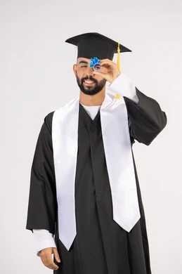Looking forward to the future after graduation, pride and joy of achieving the dream of success, portrait of a young Saudi Arabian Gulf graduate wearing graduation robes looking through his certificate of excellence, celebrating the end of the university stage, white background