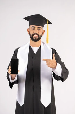 الاشارة الى الجوال، برامج وتطبيقات التعليم والدراسة اونلاين، بورتريه لشاب خريج عربي خليجي اماراتي مبتسم يرتدي القبعة وزي التخرج بتعابير السرور، الاحتفال بانتهاء المرحلة الجامعية، شاشة سوداء فارغة على الهاتف المحمول، خلفية بيضاء
