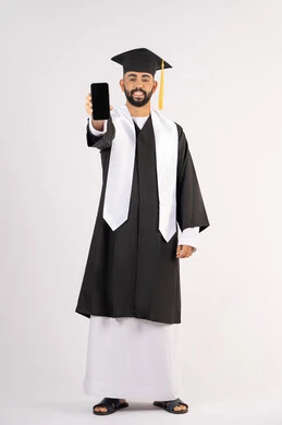 Blank black screen on mobile phone, online education and study applications, portrait of a smiling young Arab Gulf Emirati graduate wearing a cap and graduation gown with a happy expression, celebrating the end of the university stage, full body, white background