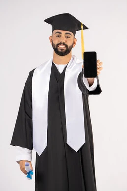 برامج وتطبيقات التعليم والدراسة اونلاين، بورتريه لشاب خريج عربي خليجي اماراتي مبتسم يرتدي القبعة وزي التخرج يمسك بيده الشهادة بتعابير السرور، الاحتفال بانتهاء المرحلة الجامعية، عرض شاشة سوداء فارغة على الهاتف المحمول، خلفية بيضاء