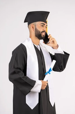 التواصل مع الأهل والأصدقاء، مفهوم الاجتهاد والتفوق، الاحتفال بإنهاء الدراسة الجامعية، استخدام التقنية الحديثة، بورتريه مقرب لشاب خريج عربي خليجي اماراتي يرتدي عباءه وقبعة التخرج يقوم بإجراء مكالمة عبر الهاتف المحمول، خلفية بيضاء