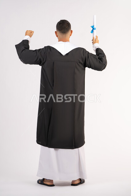Obtaining a degree, education in the United Arab Emirates, feeling proud and happy to achieve the dream of graduation, portrait from the back of a young Arab Gulf Emirati graduate wearing an abaya holding up the graduation certificate, celebrating the completion of the university stage, full body, white background