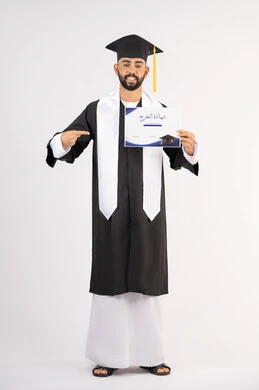 Pointing the index finger at the certificate, achieving the dream of success, university occasion and celebration, celebrating the completion of university studies, the concept of diligence and excellence, portrait of a smiling young Arab Gulf Emirati graduate wearing a graduation gown looking at the camera with an expression of happiness, full body, white background