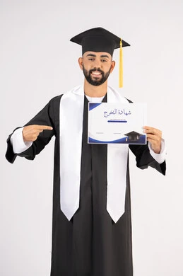 الاشارة باصبع السبابة إلى الشهادة، الوصول لحلم النجاح، مناسبة واحتفال جامعي، الاحتفال بإنهاء الدراسة الجامعية، مفهوم الاجتهاد والتفوق، بورتريه لشاب خريج عربي خليجي اماراتي مبتسم يرتدي عباءة التخرج ينظر الى الكاميرا بتعابير السعادة ، خلفية بيضاء
