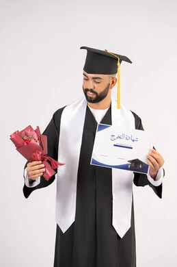إيماءات السعادة والسرور بالوصول لحلم النجاح، مناسبة واحتفال جامعي، الاحتفال بإنهاء الدراسة الجامعية، مفهوم الاجتهاد والتفوق، بورتريه لشاب خريج عربي خليجي اماراتي مبتسم يرتدي عباءة التخرج يمسك بيده باقة ورد والشهادة، خلفية بيضاء