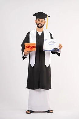 Obtaining a graduation certificate, giving gifts on occasions, celebrating the completion of university studies, gestures of happiness for reaching the dream of success, portrait of a young Arab Gulf Emirati graduate wearing graduation attire and cap, holding a certificate and gift box, full body, white background