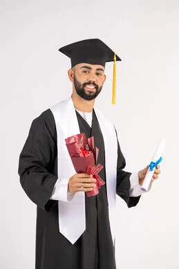 إيماءات السعادة والسرور بالوصول لحلم النجاح، مناسبة واحتفال جامعي، الاحتفال بإنهاء الدراسة الجامعية، مفهوم الاجتهاد والتفوق، بورتريه لشاب خريج عربي خليجي اماراتي مبتسم يرتدي عباءة التخرج يمسك بيده باقة ورد والشهادة، خلفية بيضاء