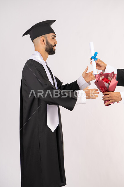 الاحتفال بالنجاح وانهاء الدراسة الجامعية، الشعور بالفخر والثقة بالنفس، استلام الشهادة بتعابير الفروح والسرور، مفهوم التفوق والاجتهاد، بورتريه من الجانب لخريج عربي خليجي اماراتي يرتدي قبعة وثوب التخرج يقوم بأخذ باقة الورد بايماءات السعادة، خلفية بيضاء