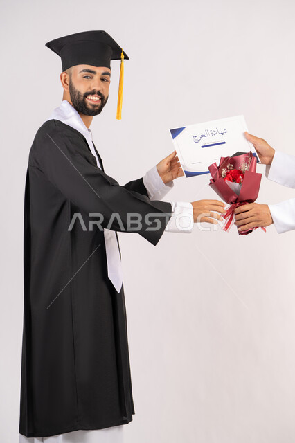 الشعور بالفخر والثقة بالنفس، استلام الشهادة بتعابير الفروح والسرور، مفهوم التفوق والاجتهاد، بورتريه من الجانب لخريج عربي خليجي اماراتي يرتدي قبعة وثوب التخرج يقوم بأخذ باقة الورد بايماءات السعادة، الاحتفال بالنجاح وانهاء الدراسة الجامعية، خلفية بيضاء