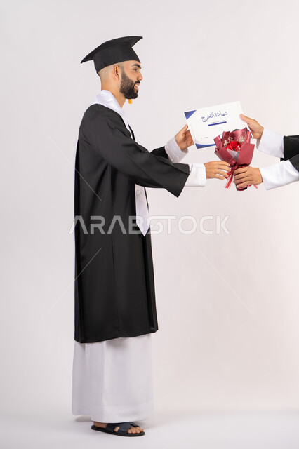 مفهوم التفوق والاجتهاد، استلام الشهادة بتعابير الفروح والسرور، بورتريه من الجانب لخريج عربي خليجي اماراتي يرتدي قبعة وثوب التخرج يقوم بأخذ باقة الورد بايماءات السعادة والسرور، الاحتفال بالنجاح وانهاء الدراسة الجامعية، صورة الجسم بالطول الكامل، خلفية بيضاء