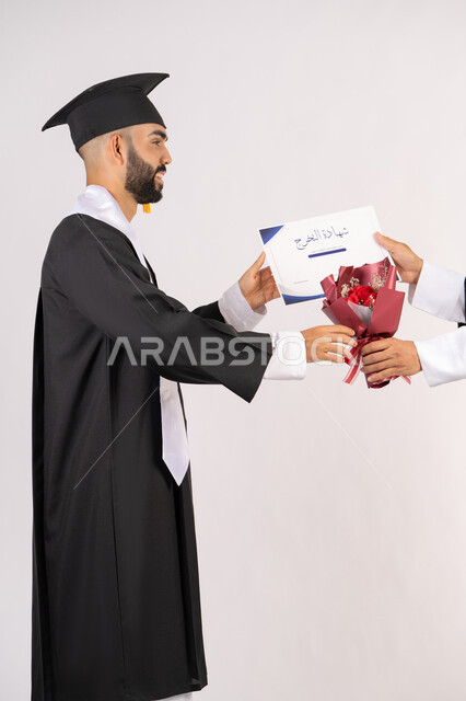 الاحتفال بالنجاح وانهاء الدراسة الجامعية، الشعور بالفخر والثقة بالنفس، استلام الشهادة بتعابير الفروح والسرور، مفهوم التفوق والاجتهاد، بورتريه من الجانب لخريج عربي خليجي اماراتي يرتدي قبعة وثوب التخرج يقوم بأخذ باقة الورد بايماءات السعادة، خلفية بيضاء