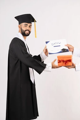 التفوق والاجتهاد والنجاح، الاحتفال بانهاء الدراسة الجامعية، تقديم الهدايا في المناسبات السعيدة، استلام الشهادة بتعابير الفروح والسرور، بورتريه من الجانب لخريج عربي خليجي اماراتي يرتدي قبعة وثوب التخرج يقوم بأخذ صندوق هدية، خلفية بيضاء