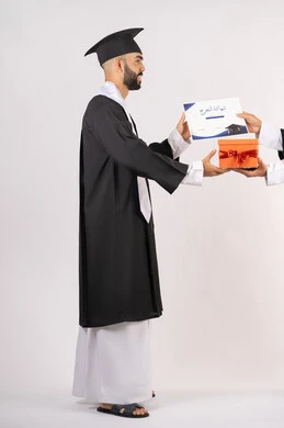 تقديم الهدايا في المناسبات السعيدة، استلام الشهادة بتعابير الفروح والسرور، مفهوم التفوق والاجتهاد، بورتريه من الجانب لخريج عربي خليجي اماراتي يرتدي قبعة وثوب التخرج يقوم بأخذ صندوق هدية،  الاحتفال بالنجاح وانهاء الدراسة الجامعية، الجسم بالطول الكامل، خلفية بيضاء