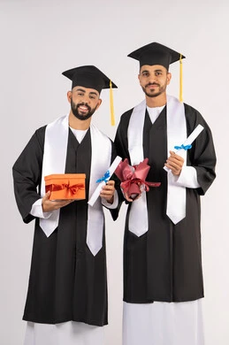 الحصول على شهادة التخرج، تقديم الهدايا في المناسبات السعيدة، الاحتفال بإنهاء الدراسة الجامعية،  بورتريه لشاب خريج عربي خليجي اماراتي يرتدي عباءه وقبعة التخرج يقف مع صديقه ويمسكان بيديهما الشهادة مع باقة ورد مع صندوق هدية، مناسبة واحتفال جامعي، خلفية بيضاء
