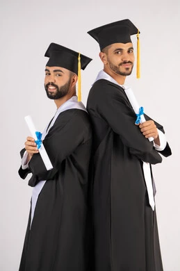 مناسبة واحتفال جامعي، الاحتفال بإنهاء المرحلة الجامعية، التقاط صور شخصية بثياب التخرج، بورتريه لشابين خريجين عربيين خليجيين اماراتيين مبتسمين يرتديان القبعة وعباءة التخرج ينظران الى الكاميرا بتعابير السرور، مفهوم التفوق والنجاح والاجتهاد، خلفية بيضاء