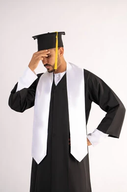 الارهاق والتعب بعد الاجتهاد والمثابرة، الانتهاء من مرحلة الدراسة الجامعية بعد عناء، بورتريه لشاب خريج عربي خليجي اماراتي يرتدي القبعة وزي التخرج يضع يده على رأسه بتعابير اليأس،  انتظار النتائج بفارغ الصبر، خلفية بيضاء