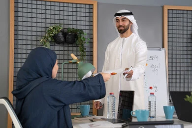 توزيع اوراق البيانات على الحضور، التفاهم والتعاون بين الزملاء ووضع الخطط الاستراتيجية لتحقيق الأهداف، استخدام السبورة لضمان فهم واضح وشامل، عقد اجتماع داخل مقر الشركة، مجموعة من الموظفين العرب الخليجيين الاماراتيين يتعلمون اساليب العمل والتطوير المهني