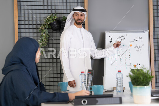 Collaboration and understanding among colleagues, developing strategic plans to achieve goals, using the whiteboard to ensure a clear and comprehensive understanding of the business, holding a meeting at the company's headquarters, a group of Arab Gulf Emirati employees learning work methods and professional development, team spirit and teamwork.