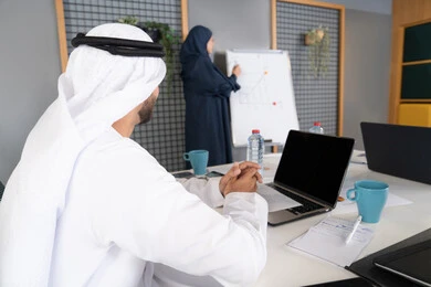 روح الفريق الواحد والعمل الجماعي، التعاون والتفاهم بين الزملاء، التخطيط الاستراتيجي والتنظيم لتحقيق الأهداف، استخدام السبورة لضمان فهم واضح وشامل للاعمال، عقد اجتماع داخل مقر الشركة، مجموعة من الموظفين العرب الخليجيين الاماراتيين يتعلمون اساليب العمل والتطوير المهني