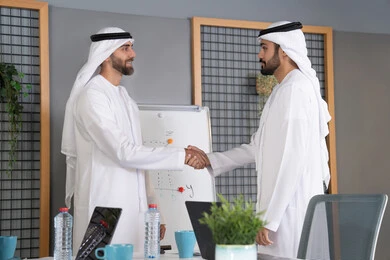 الترحيب والاستقبال ببشاشة، مكاتب وشركات في الامارات العربية المتحدة، عقد اتفاقيات وصفقات جديده, الإتفاق على المشاريع التجارية، رجال عرب خليجيين اماراتيين يقومون بمصافحة بعضهم داخل مقر العمل، الشراكة والتعاون في إنجاز المهام