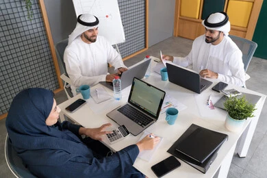 Integrating work with technology, developing Emirati companies, following up on business projects, a group of Emirati Gulf Arab employees completing work tasks via a computer inside the company's headquarters, focusing and working accurately to achieve goals.