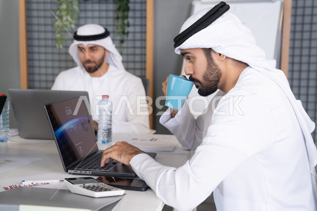 Integrating work with technology, developing Emirati companies, following up on business projects, a group of Emirati Gulf Arab employees completing work tasks via a computer inside the company's headquarters, focusing and working accurately to achieve goals.