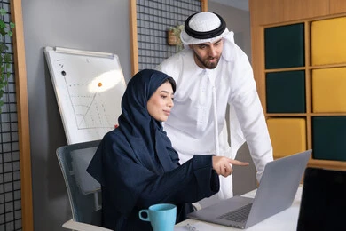تدريب الموظفين الأساليب الجديدة في العمل لتحقيق أهداف الشركة، دمج العمل مع التقنية والتكنولوجيا، زميلان عربيان خليجيان اماراتيان يقومان بإنجاز المهام عبر الحاسوب المحمول، الاشارة الى اللابتوب، العمل الجماعي وروح الفريق الواحد، بيئة العمل المريحة في الامارات
