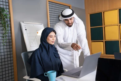 دمج العمل مع التقنية والتكنولوجيا، زميلان عربيان خليجيان اماراتيان يقومان بإنجاز المهام عبر الحاسوب المحمول، الاشارة الى اللابتوب، العمل الجماعي وروح الفريق الواحد، بيئة العمل المريحة في الامارات، تعليم الموظفين الأساليب الجديدة في العمل لتحقيق أهداف الشركة