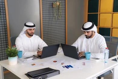 تطور الشركات الاماراتية، متابعة مشاريع الأعمال، رجلان خليجيان عربيان اماراتيان يرتديان الكندروة والغترة يقومان بإنجاز مهام العمل عبر جهاز الحاسوب، تعابير وايماءات التركيز، العمل على الخطة لتحقيق اهداف الشركة، دمج العمل مع التقنية والتكنولوجيا