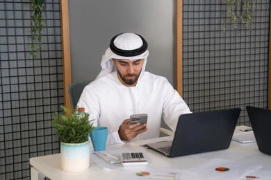 ايماءات وتعابير التركيز، العمل على الخطة لتحقيق اهداف الشركة، دمج العمل مع التقنية والتكنولوجيا، تطور الشركات الاماراتية، متابعة مشاريع الأعمال، رجل خليجي عربي اماراتي يرتدي الكندروة والغترة يقوم بإنجاز مهام العمل عبر جهاز الحاسوب