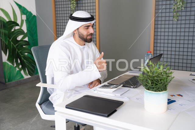 Online business meetings, integrating work with technology, UAE companies, live streaming and video calls, waving and greeting each other remotely, an Emirati Gulf Arab man wearing a ghutra and kandura using a laptop, concluding external business deals