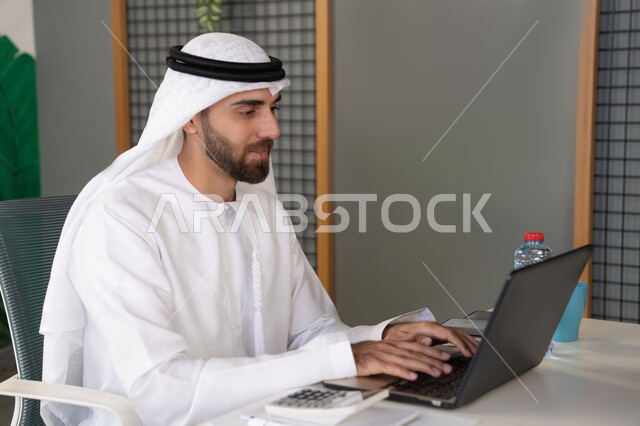 بث مباشر ومكالمات فيديو, التلويح باليد والسلام عن بعد، رجل عربي خليجي اماراتي يرتدي الغترة والكندورة يقوم باستخدام جهاز الحاسوب المحمول, عقد صفقات عمل خارجية، اجتماعات عمل أونلاين، دمج العمل بالتقنية والتكنولوجيا، شركات الامارات العربية المتحدة