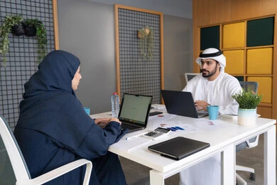 The concept of dialogue and exchange of opinions in business plans, conducting a recruitment and employment interview, an Emirati Gulf Arab man wearing a ghutra and kandura inside the office conducting a job interview with a female employee, office administrative professions and jobs in the Emirates, equality between women and men