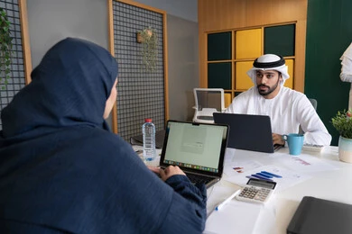 المساواة بين المرأة والرجل، مفهوم التحاور وتبادل الأراء في خطط إنجاز الأعمال، إجراء مقابلة التعيين والتوظيف، رجل عربي خلجي إماراتي يرتدي الغترة والكندورة داخل المكتب يقوم بإجراء مقابلة عمل مع موظفة، مهن ووظائف إدارية مكتبية في الإمارات