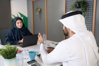 المساواة بين المرأة والرجل، مفهوم التحاور وتبادل الأراء في خطط إنجاز الأعمال، إجراء مقابلة التعيين والتوظيف، رجل عربي خلجي إماراتي يرتدي الغترة والكندورة داخل المكتب يقوم بإجراء مقابلة عمل مع موظفة، مهن ووظائف إدارية مكتبية في الإمارات