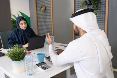 مفهوم التحاور وتبادل الأراء في خطط إنجاز الأعمال، إجراء مقابلة التعيين والتوظيف، رجل عربي خلجي إماراتي يرتدي الغترة والكندورة داخل المكتب يقوم بإجراء مقابلة عمل مع موظفة، مهن ووظائف إدارية مكتبية في الإمارات، المساواة بين المرأة والرجل